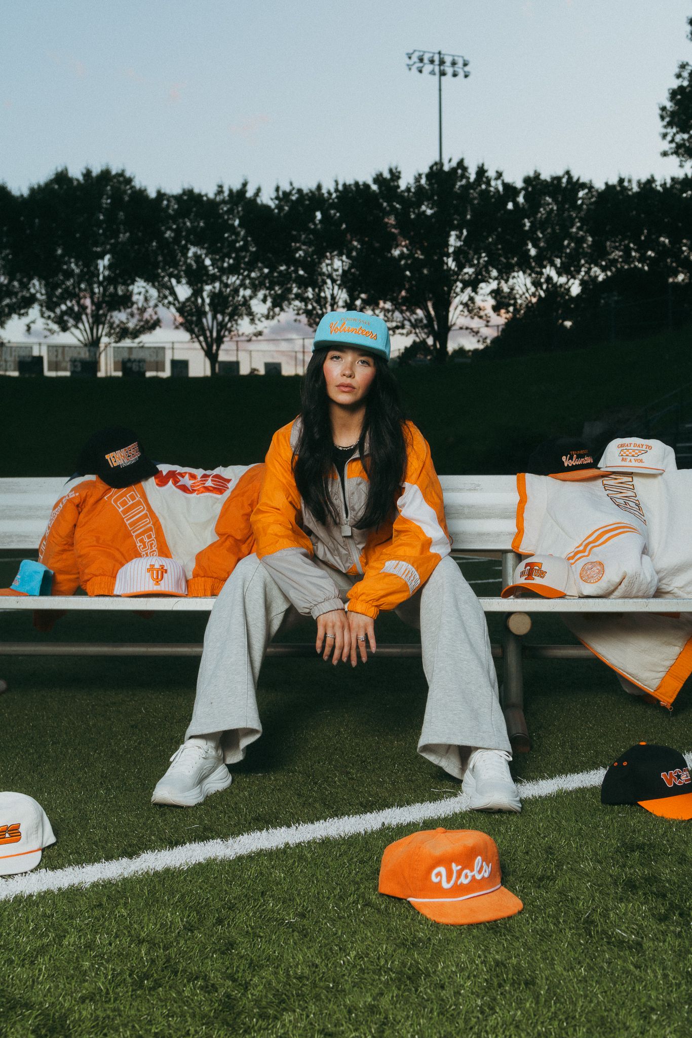 Woman sitting on bleachers surrounded by orange Tennessee Volunteers Vols caps and gear.