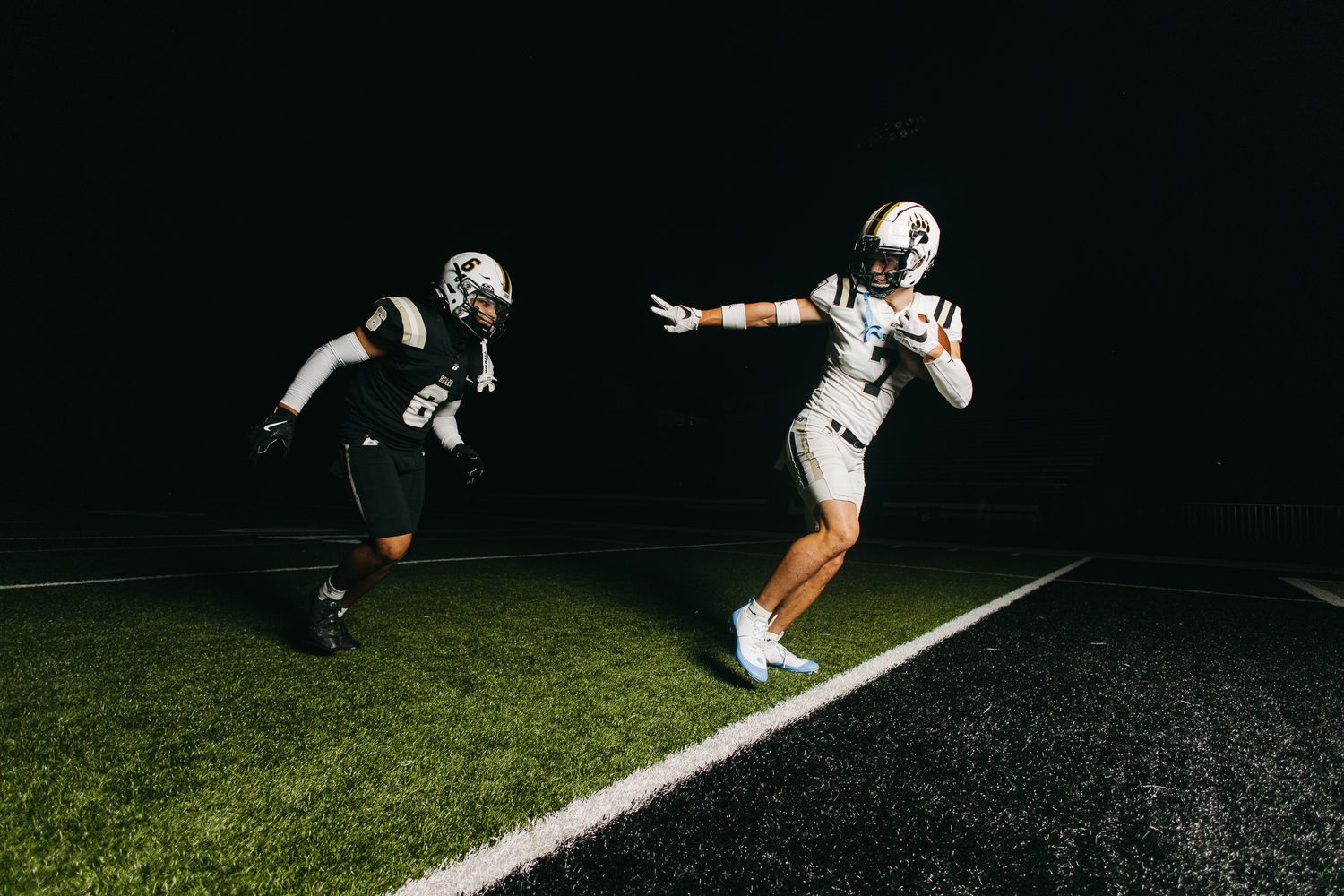 Football player catches a pass at night under stadium lights while a defender pursues during a game.