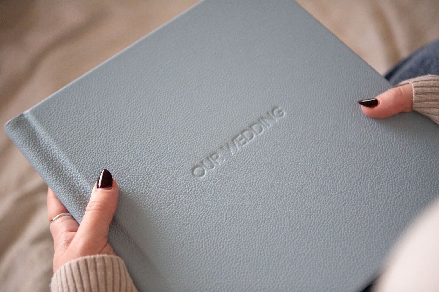 Hands with black nail polish hold a soft grey leather wedding photo album by Luxe Albums.