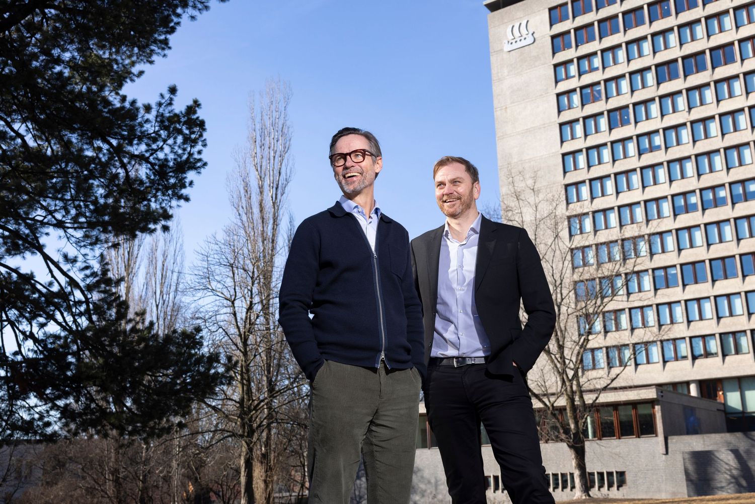 Two professional men standing outdoors near a modern office building on a sunny day.