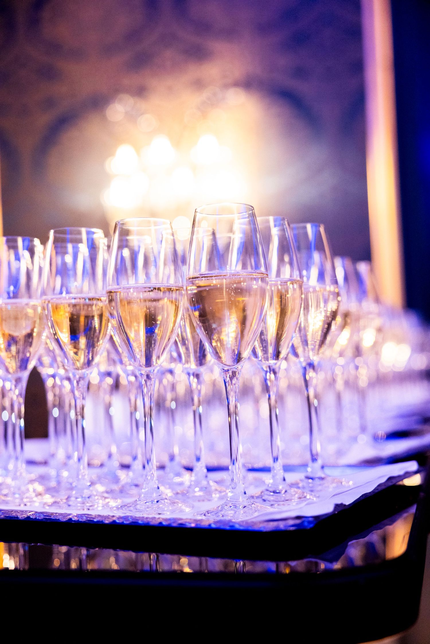 Champagne glasses arranged in rows on a dark surface with blue ambient lighting creating an elegant party atmosphere. Grand Hotel