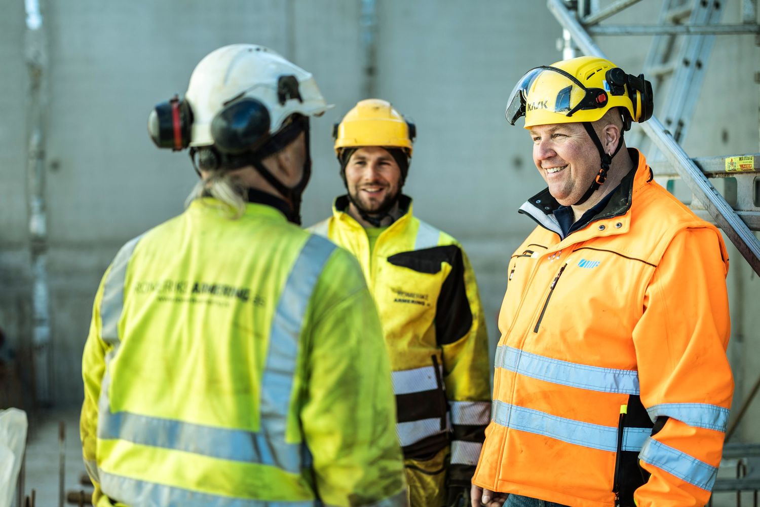 Three construction workers in hi-vis jackets and helmets having a discussion at a construction site.