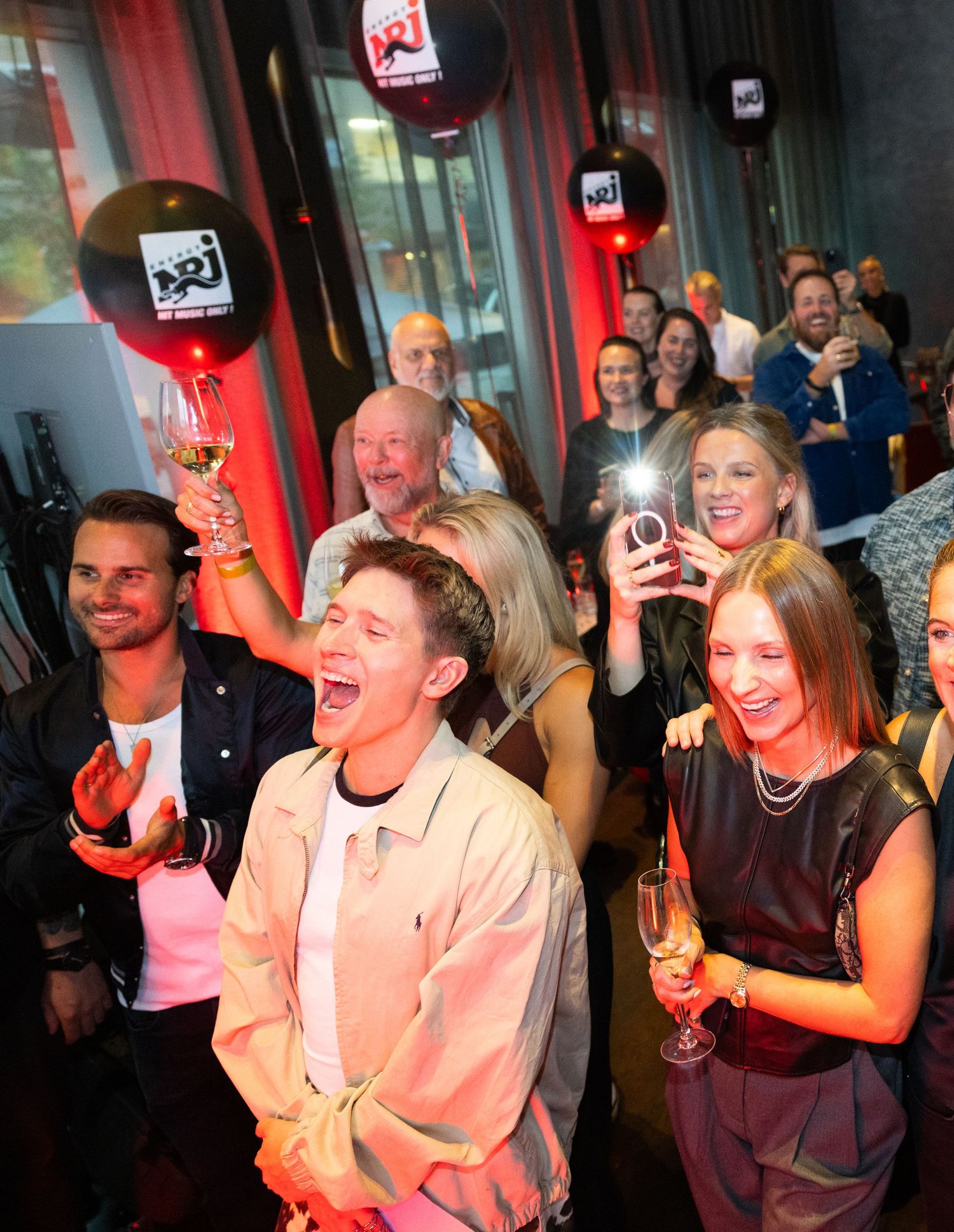 Excited crowd celebrating at NRJ radio event holding champagne glasses and balloons.