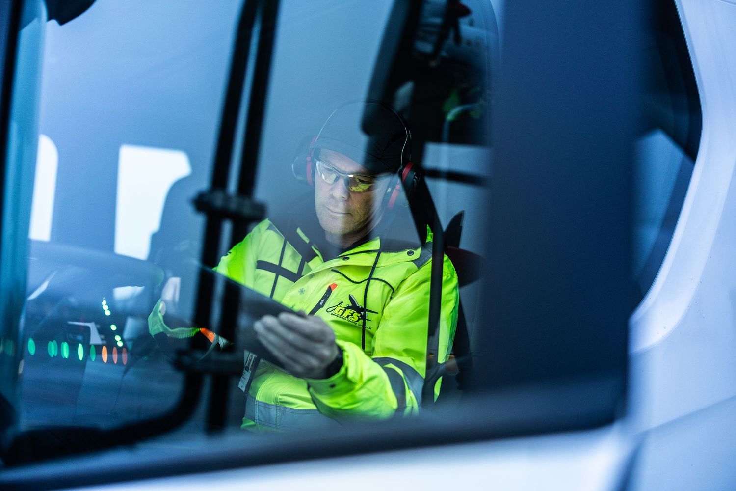 Airport ground crew worker in yellow safety vest checks documents inside truck cab.