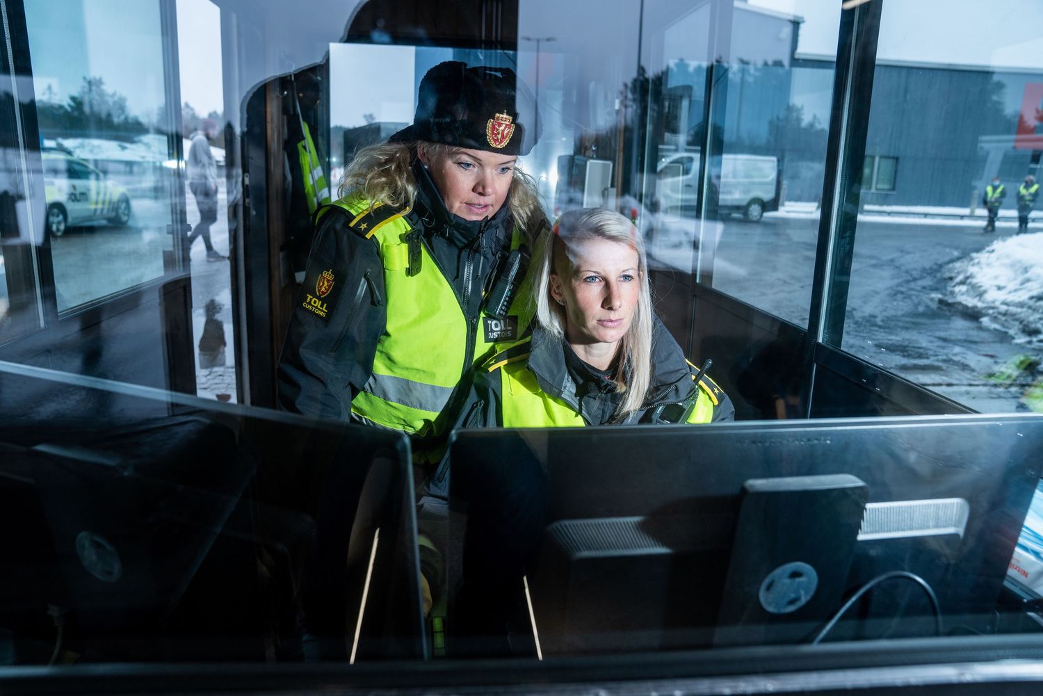 Two women in security uniforms examine a computer screen at a border control checkpoint.