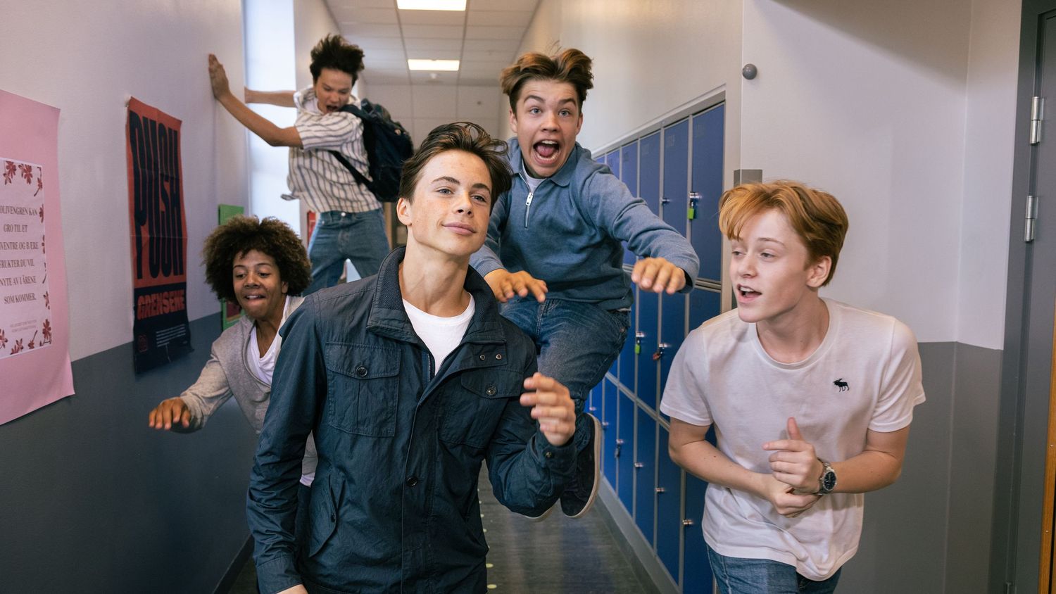 Group of energetic young people running through a school hallway with lockers.