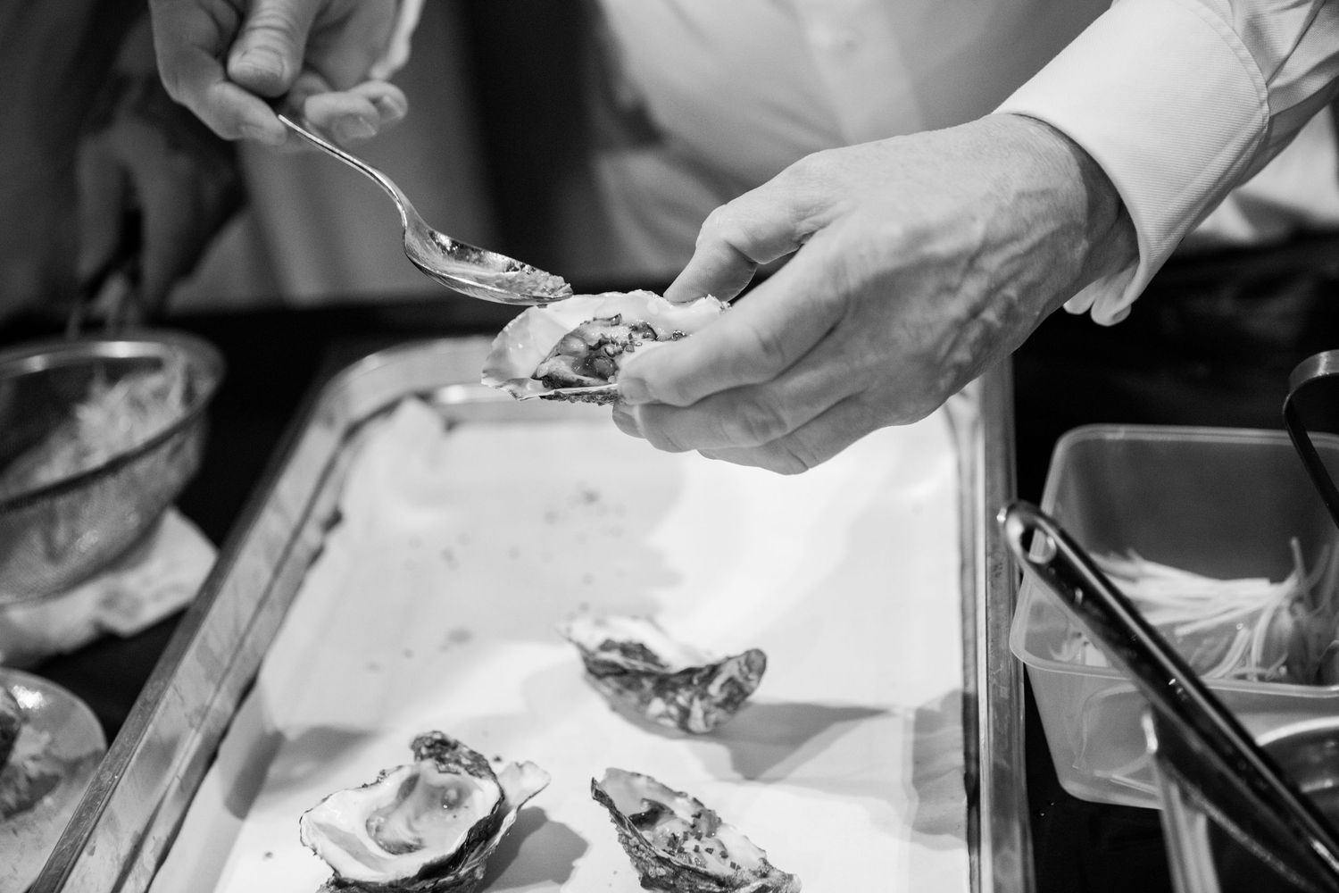 Chef's hands carefully garnishing fresh oysters on the half shell at a catering event.