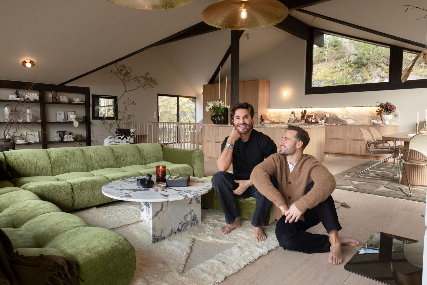 Two men relaxing in a stylish modern living room with green sofa and vaulted ceiling.