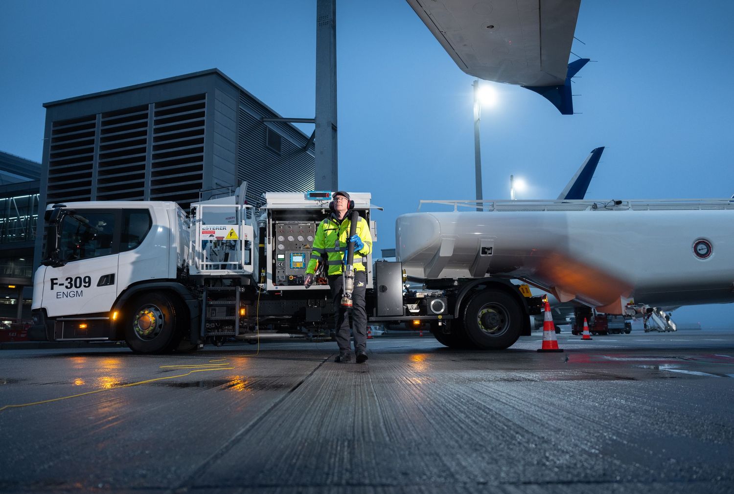 Airport fuel truck worker in high-visibility gear refuels a commercial aircraft at night.