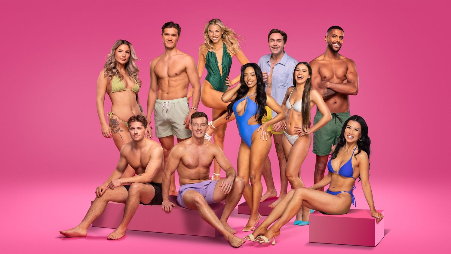 Group of attractive young people in swimwear posing together on a bright pink background.