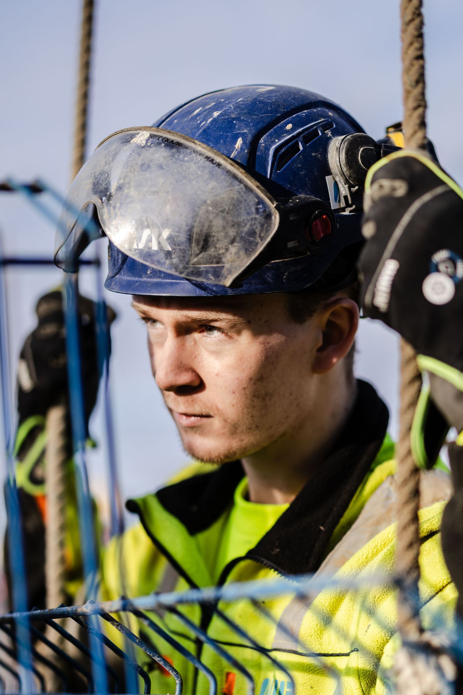 Construction worker in blue KASK helmet with visor at a building site wearing yellow high-visibility jacket.