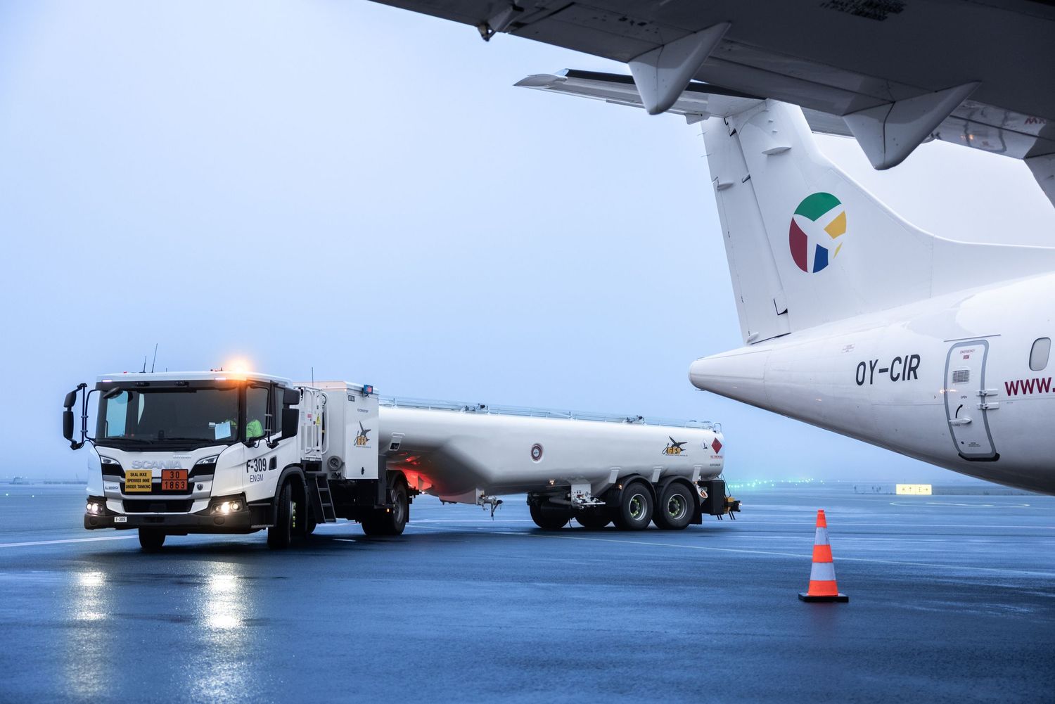 Aviation fuel tanker truck refueling commercial aircraft on airport tarmac at dusk.