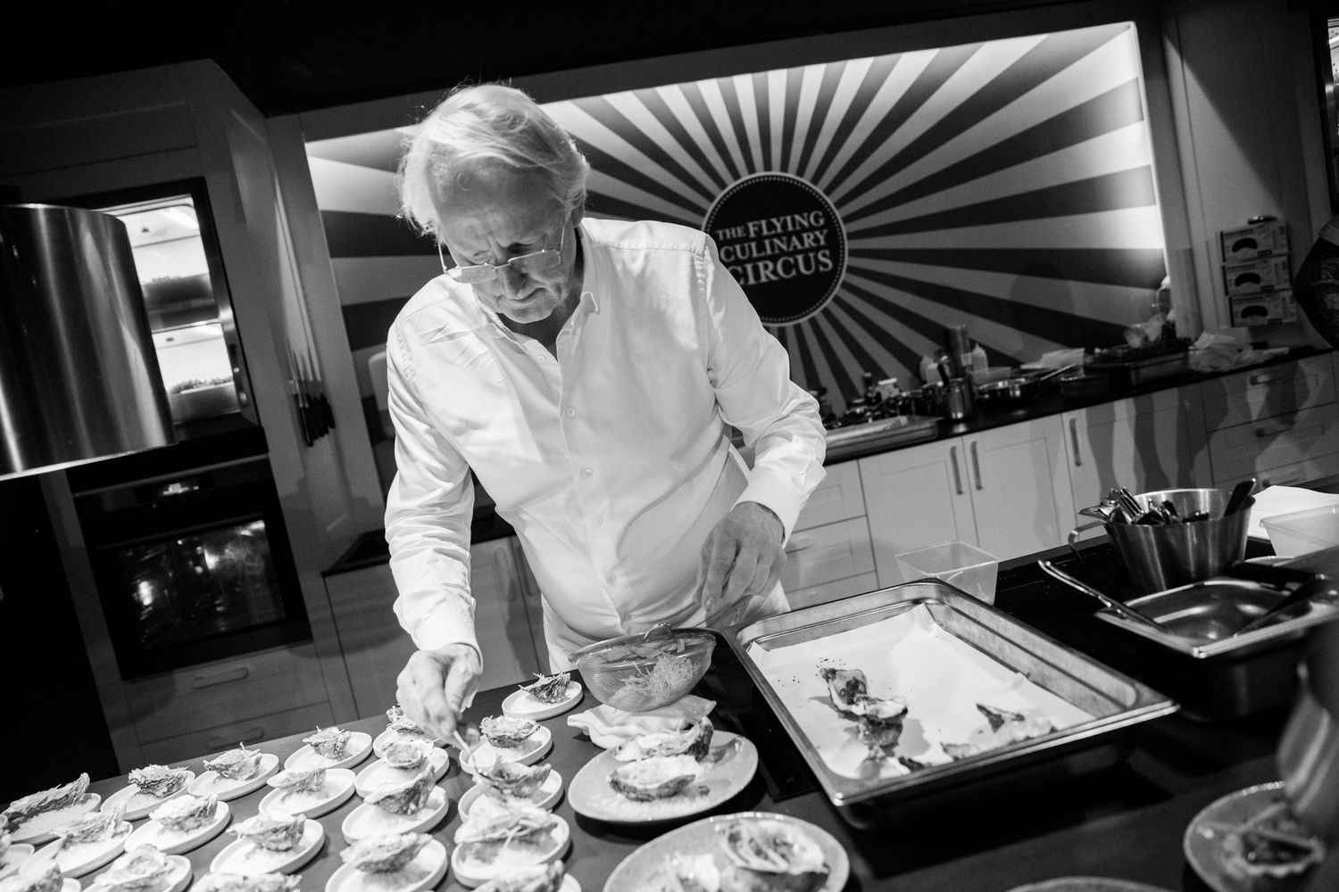 Chef preparing multiple dessert plates at a Flying Culinary Circus event in a professional kitchen.