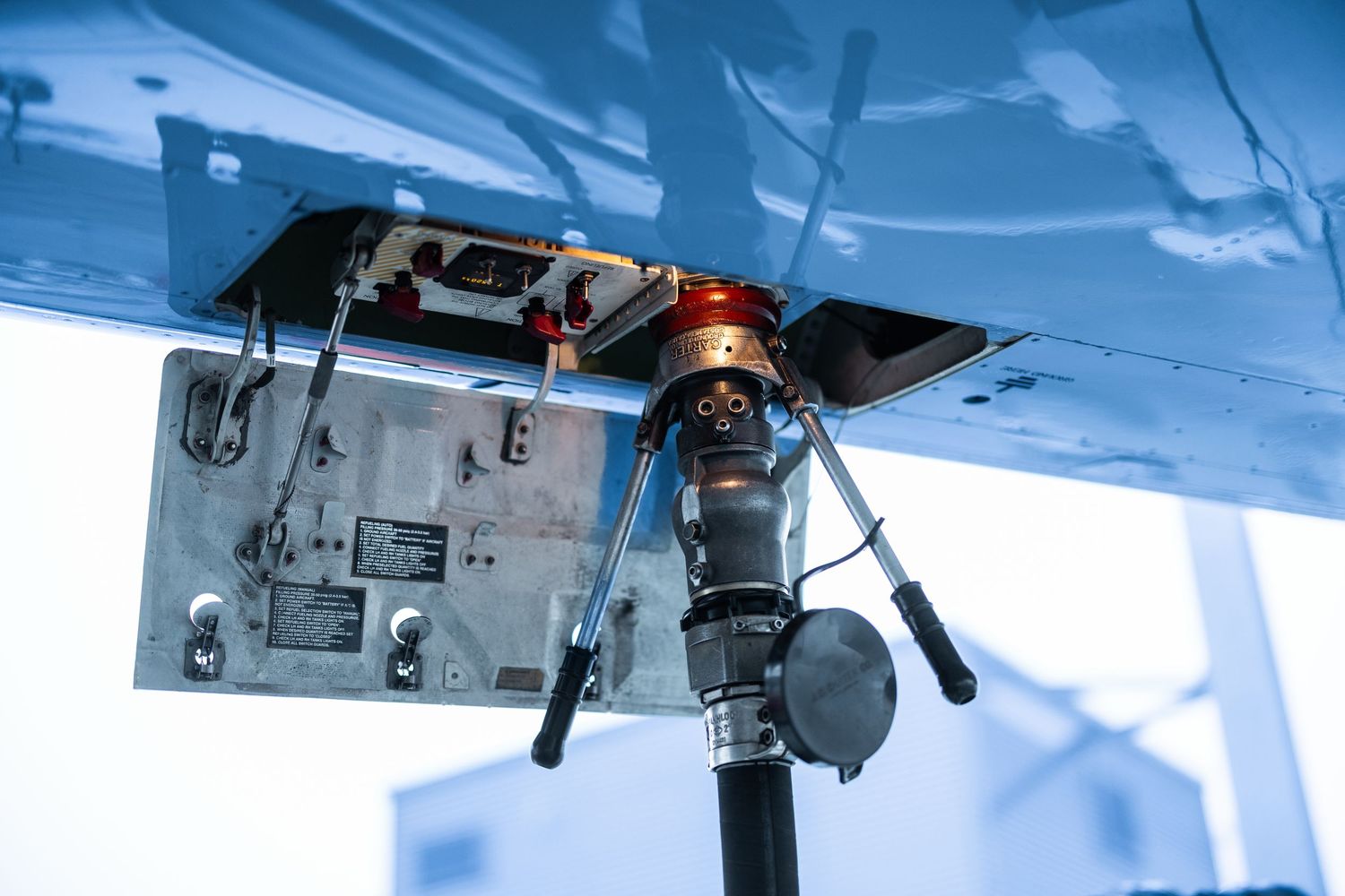 Close-up of aircraft underbelly fuel port with refueling nozzle attached.