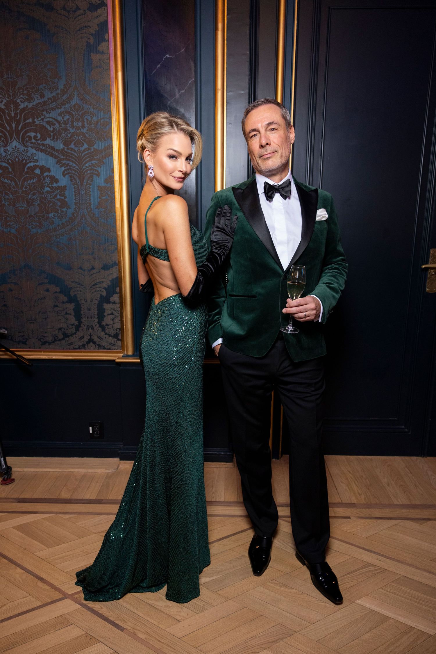 Katrine Sørland og Andreas Holck in formal attire pose at gala event, wearing emerald green sequin gown and velvet tuxedo jacket.