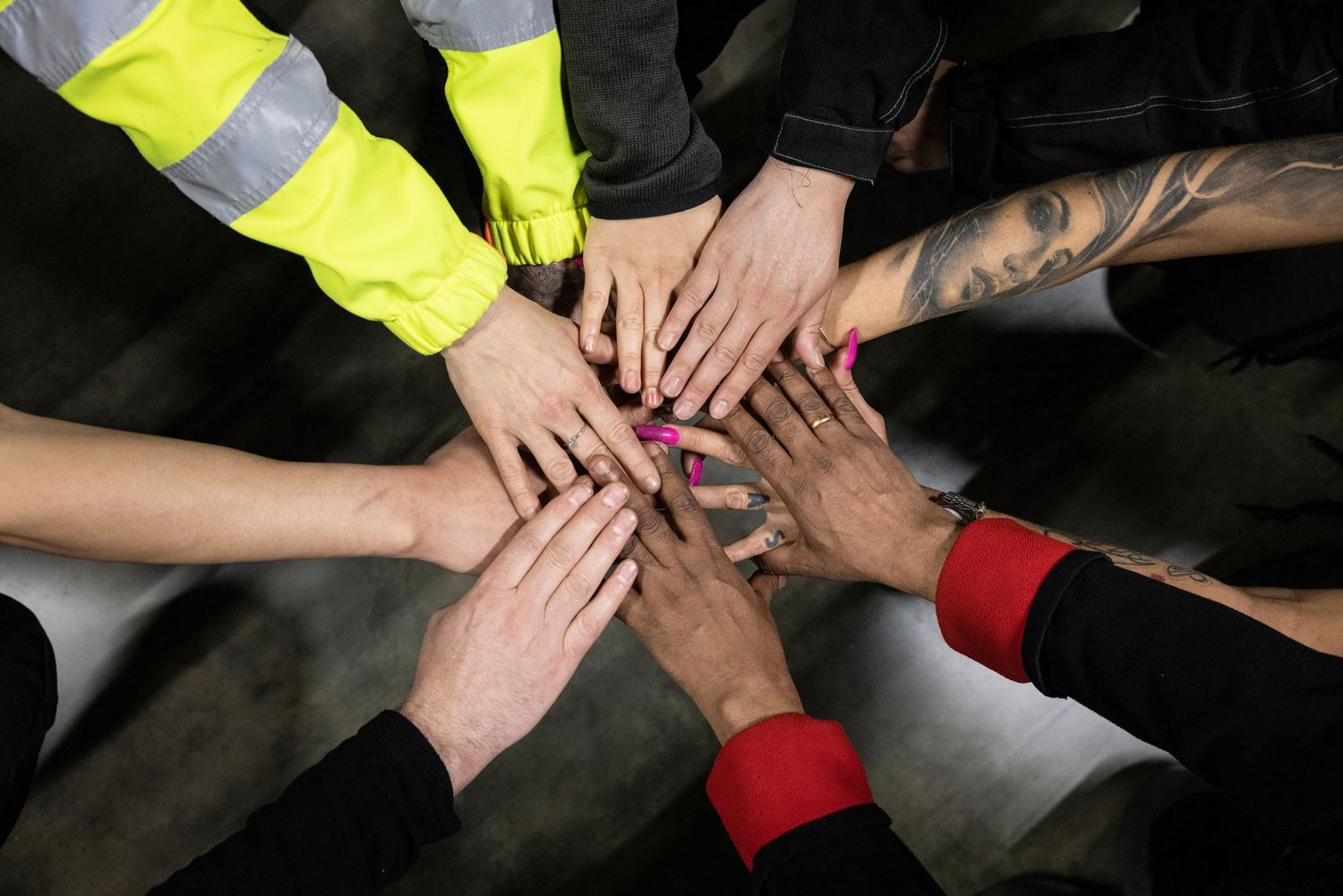 Diverse group of people stacking hands together in a teamwork gesture, viewed from above in a circle.