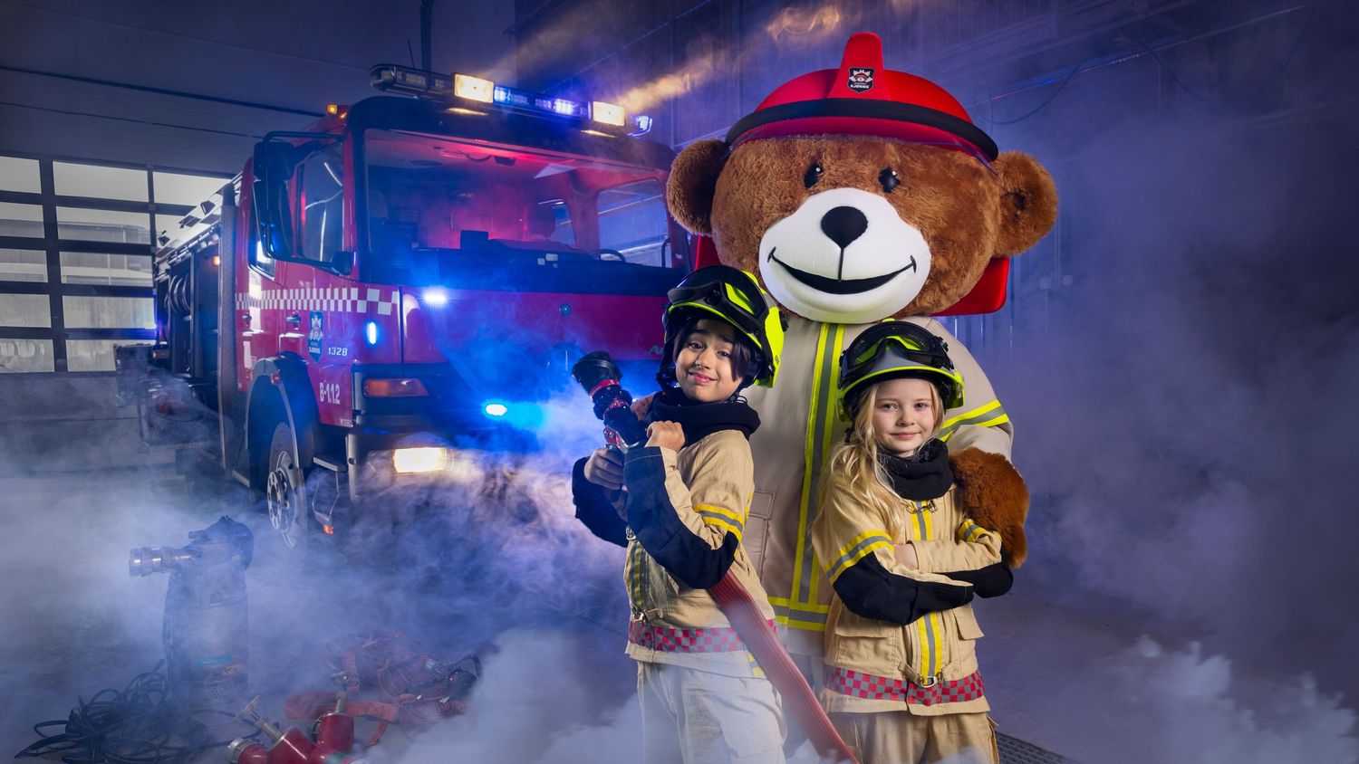 Children pose with a firefighter teddy bear mascot in front of a fire truck surrounded by smoke.