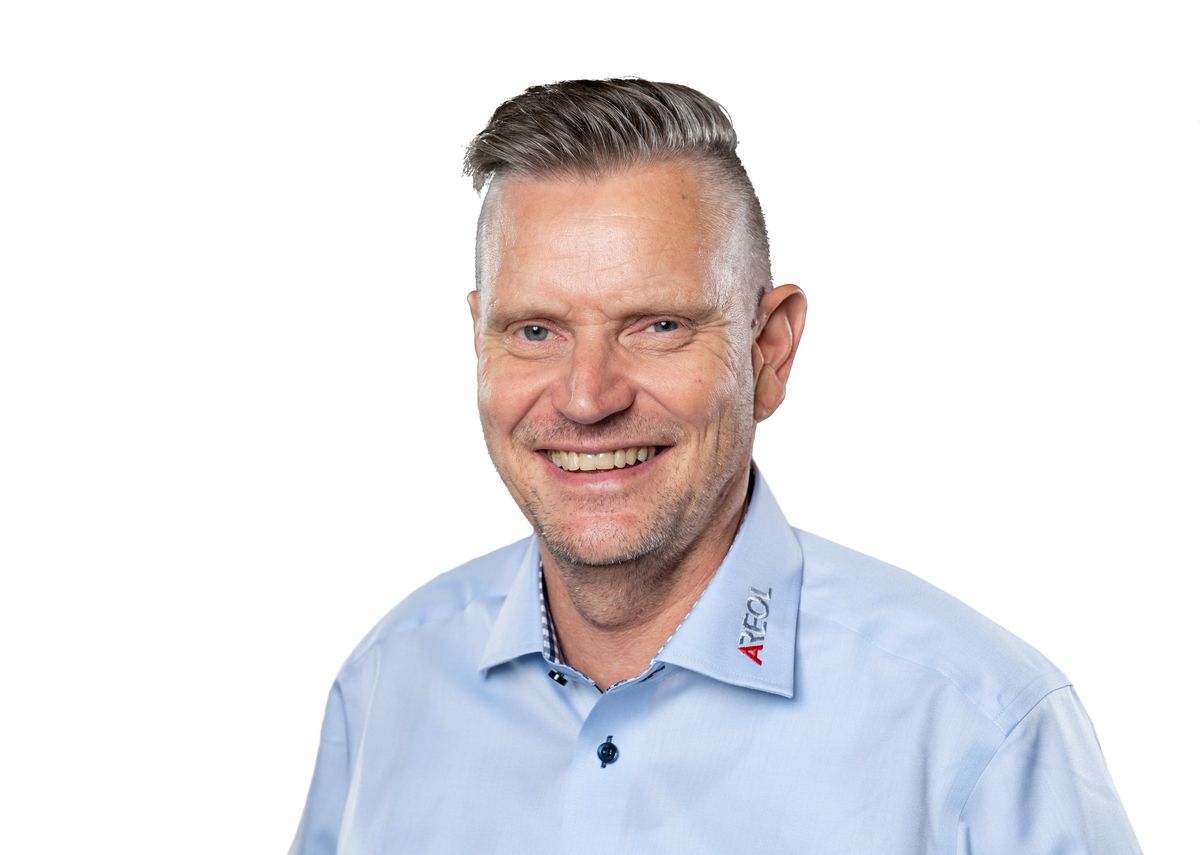 Smiling middle-aged man with short gray hair wearing a light blue shirt on white background.