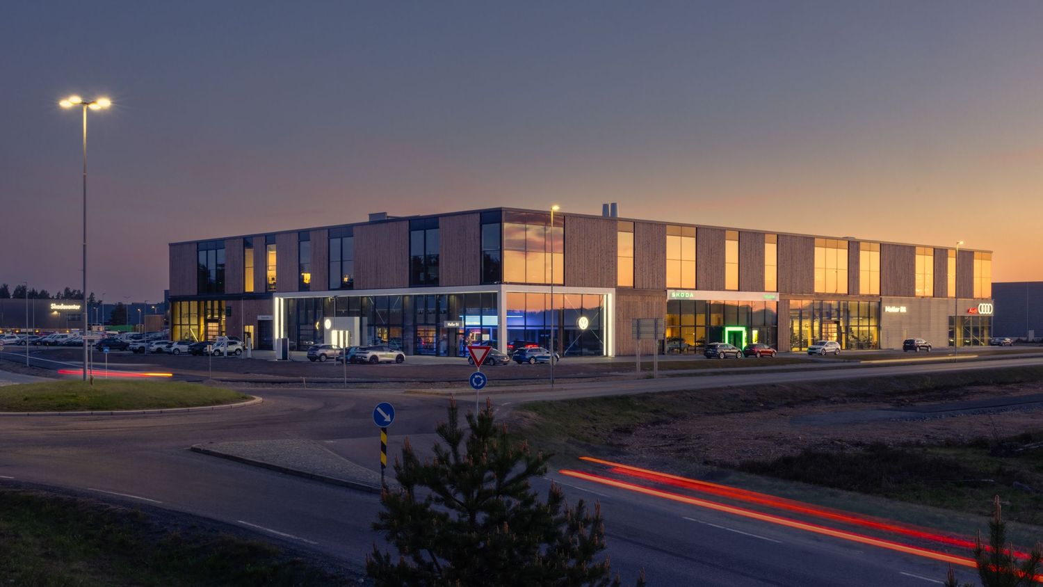 Modern commercial building exterior illuminated at dusk with light trails from passing traffic nearby.