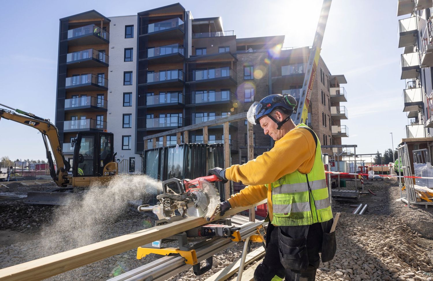 Construction worker in yellow vest cutting material with circular saw at an urban building site on sunny day.