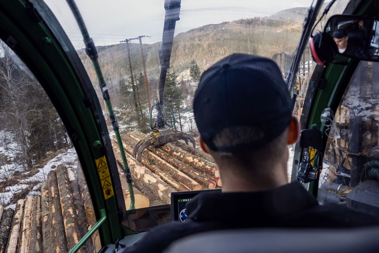 Operator inside harvester cab viewing loaded timber logs from above.