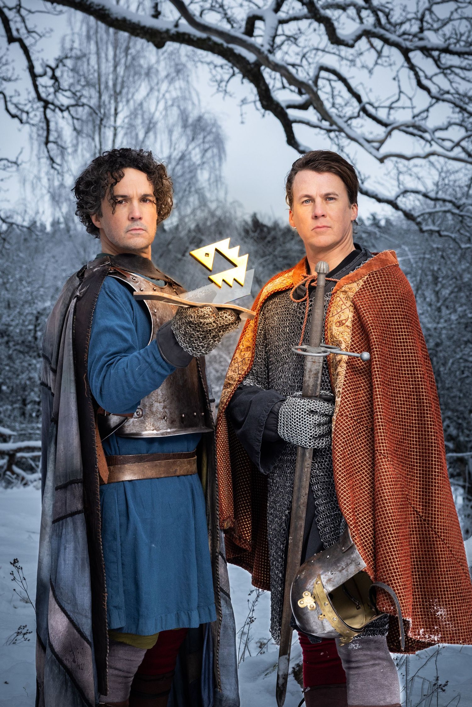 Two men in medieval knight costumes posing seriously in a snowy winter landscape.