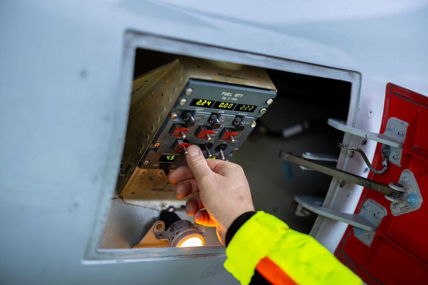 Airport ground crew operating aircraft fueling panel controls in hi-vis safety jacket.