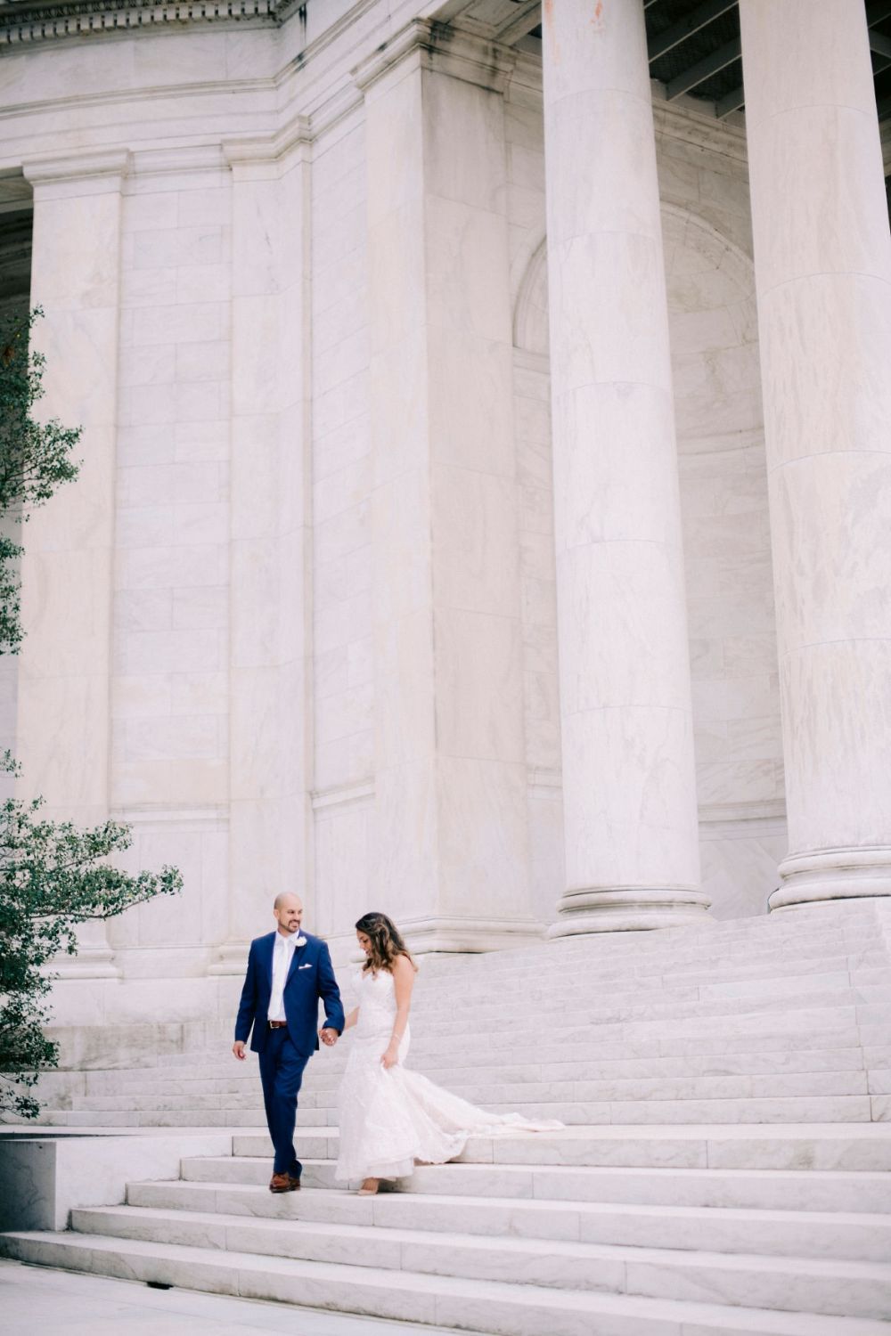 A couple in wedding attire poses on the grand white marble steps of the Jefferson Memorial in Washington DC.