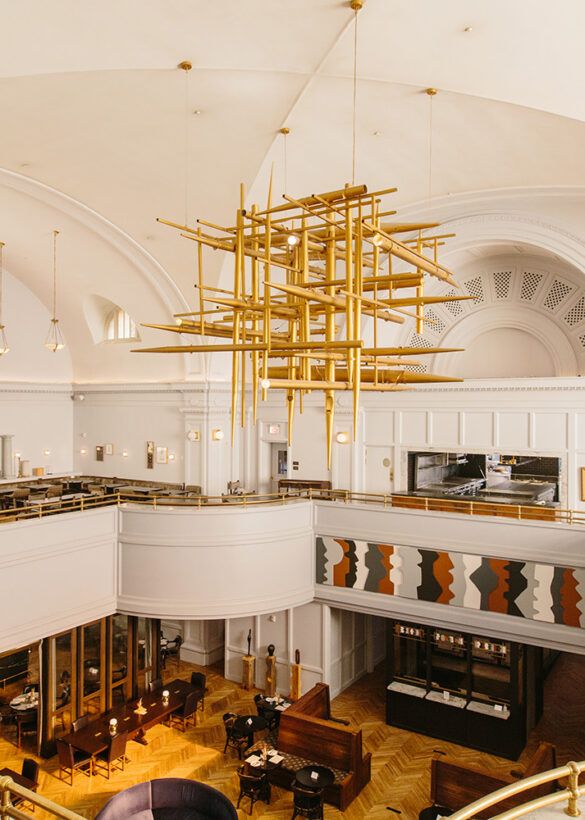 Modern church interior at the Line Hotel in Washington DC with dramatic gold geometric chandelier and curved white balcony and wooden pews.