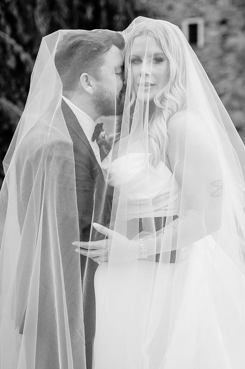 A romantic black and white wedding photo showing a couple sharing an intimate moment under a delicate veil.