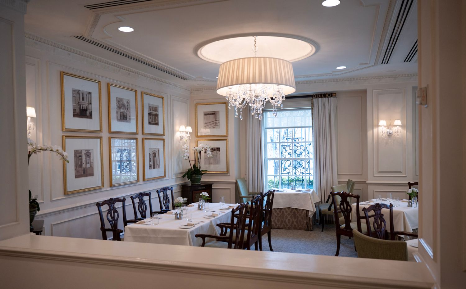 Elegant dining room with crystal chandelier, white wainscoting, framed artwork, and traditional dark wood chairs.