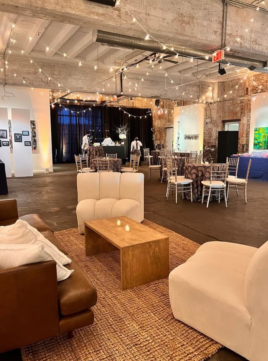 Interior of the Longview Gallery with a wooden table and cushioned chairs with hung lights above, getting ready for a wedding.