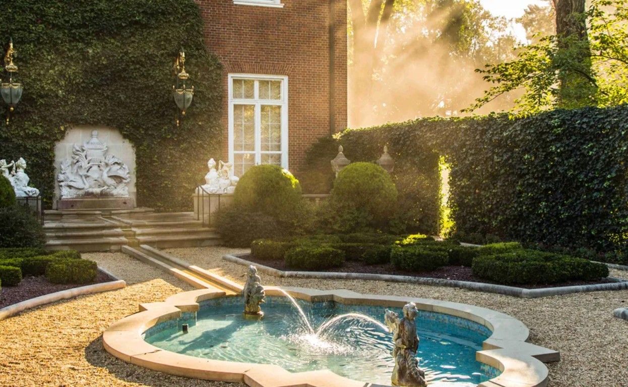 A serene backyard pool area with stone pavers and landscaping surrounded by lush greenery at sunset.