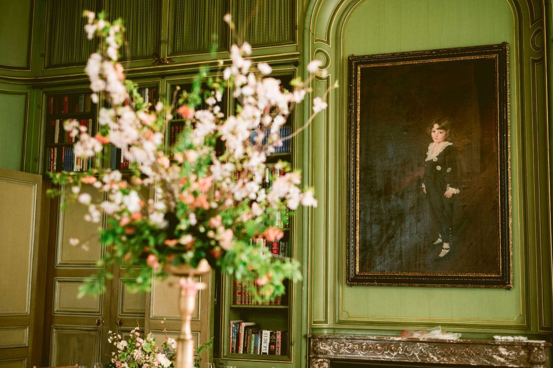 Elegant living room with ornate gold frames, floral arrangements, and green damask wallpaper in a historic mansion.