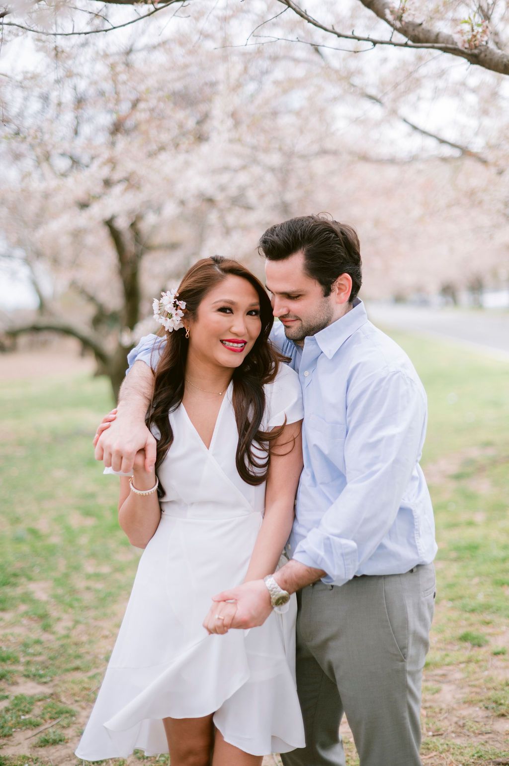 Romantic couple laughing and embracing under blooming cherry blossom trees in springtime.