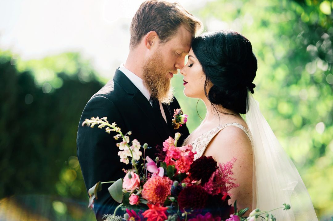 A romantic wedding moment outdoors with a vibrant red and pink bouquet against a soft green natural background.