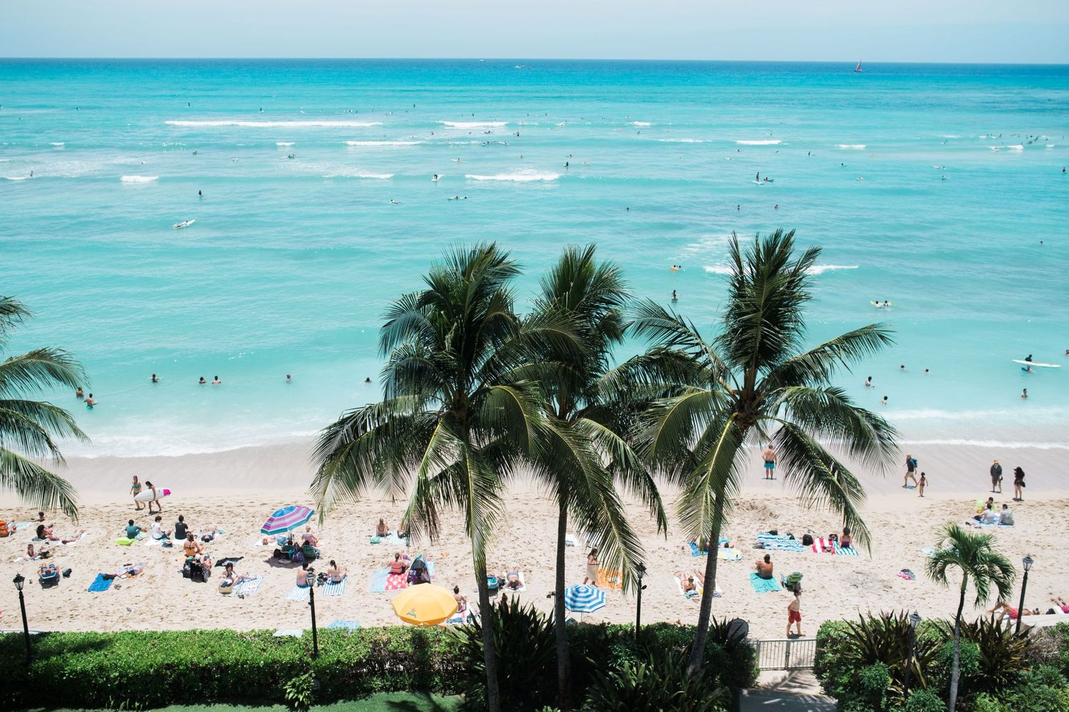 Panoramic view of a tropical beach with turquoise waters, palm trees, and beachgoers enjoying the sunny day.