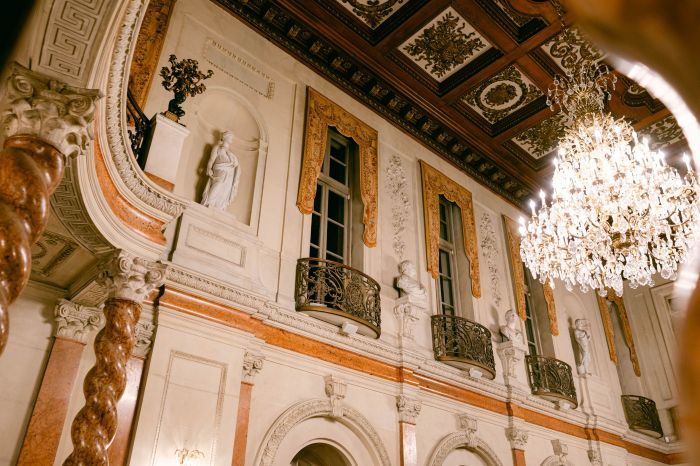 Ornate baroque ballroom interior with crystal chandeliers, gilded details, and mirrored walls reflecting warm lighting.
