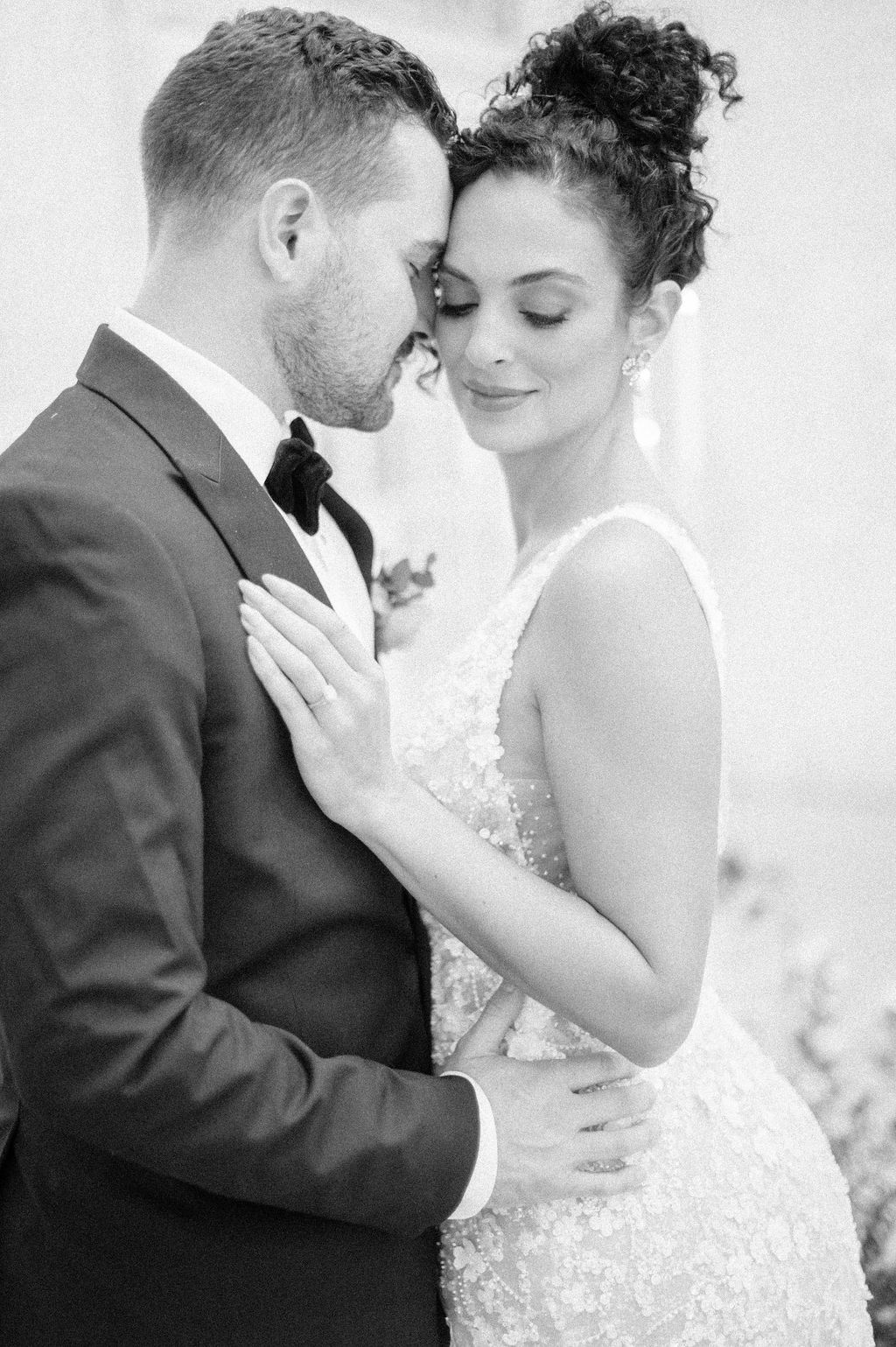 A romantic black and white wedding portrait of a couple embracing in formal attire.