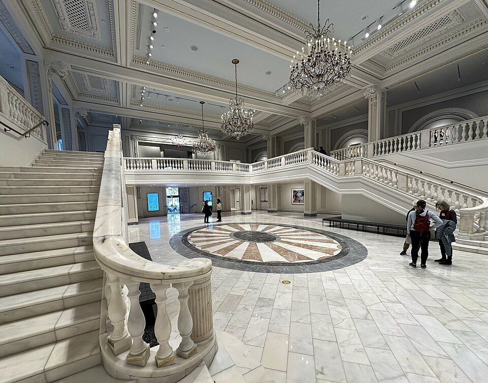 Elegant white marble interior with ornate crown molding, crystal chandeliers, and grand staircases in a luxurious venue.