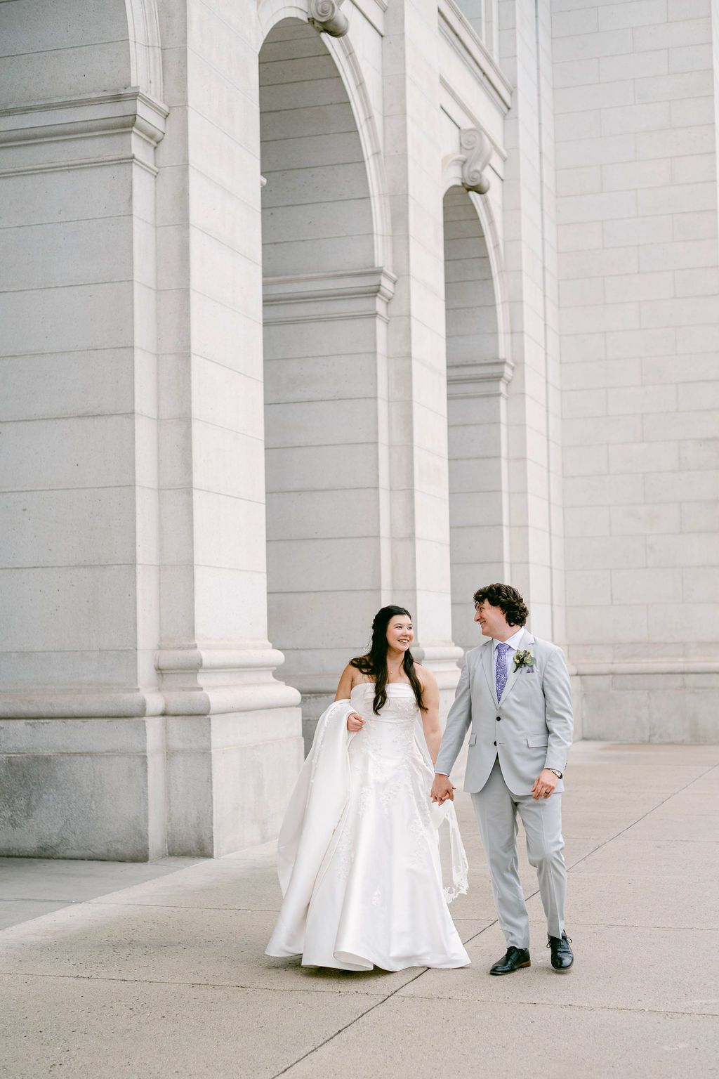 A couple shares romantic moments in front of white stone columns during their wedding photoshoot.