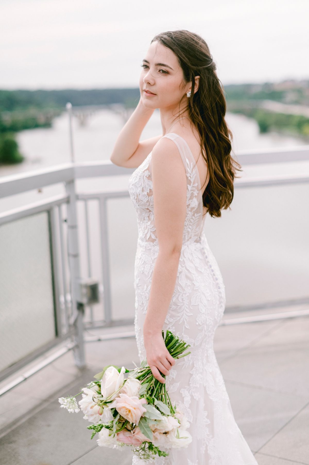 A bride in a white lace wedding dress holds a delicate bouquet while posing on a balcony atop Sequoia Restaurant in Washington DC.