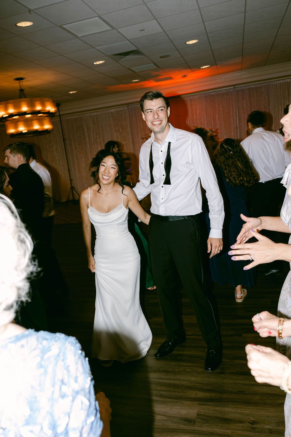 Couple dancing together at a Belmont Country Club wedding reception on wooden dance floor with warm lighting and other guests around them.