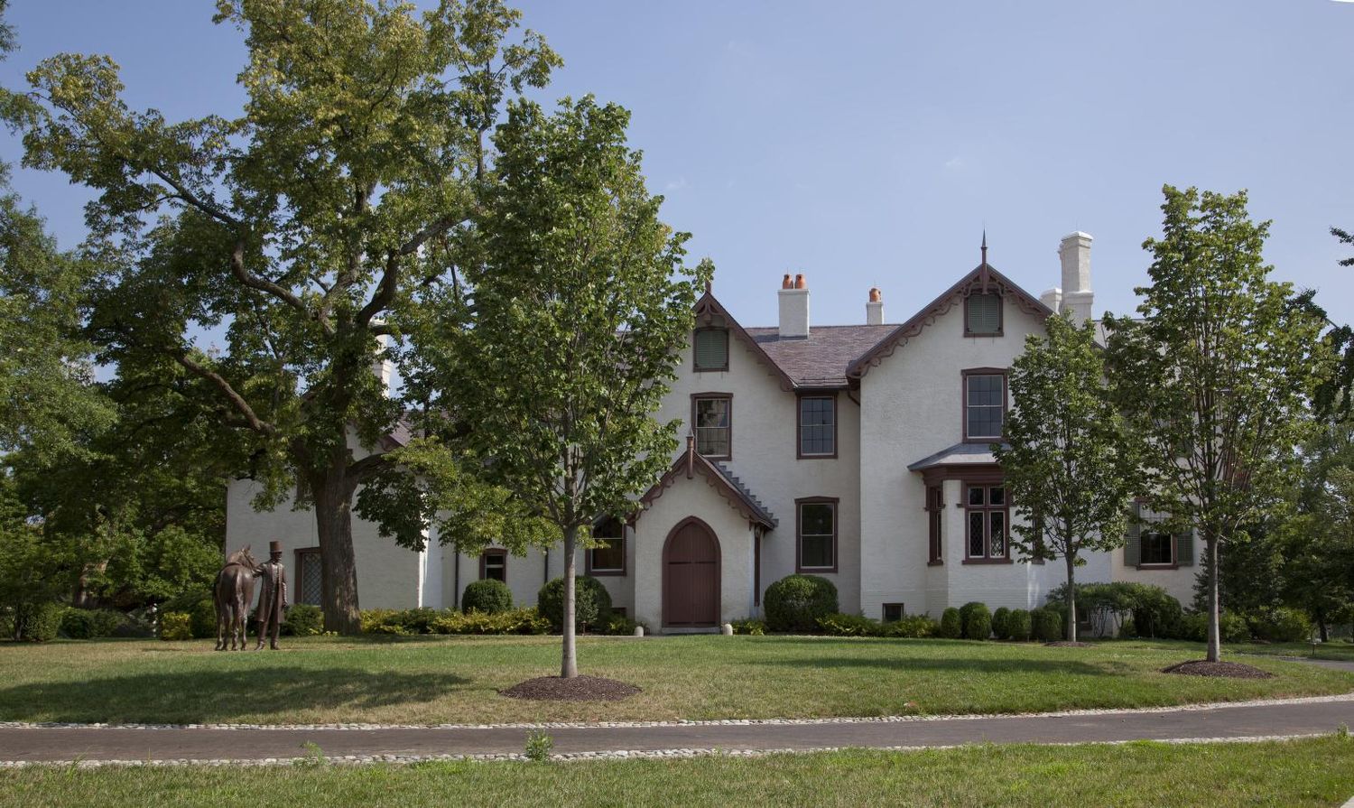 A panoramic view of white rural church buildings with trees and green grass surroundings.
