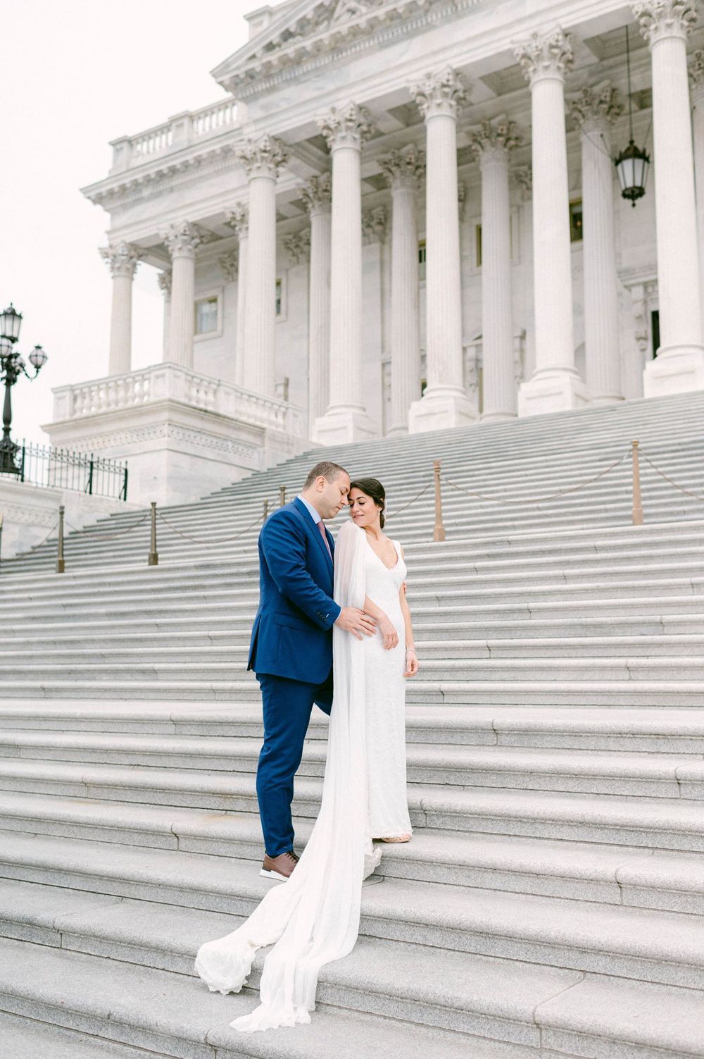 Couple shares romantic moments on grand white marble steps of a historic government building.