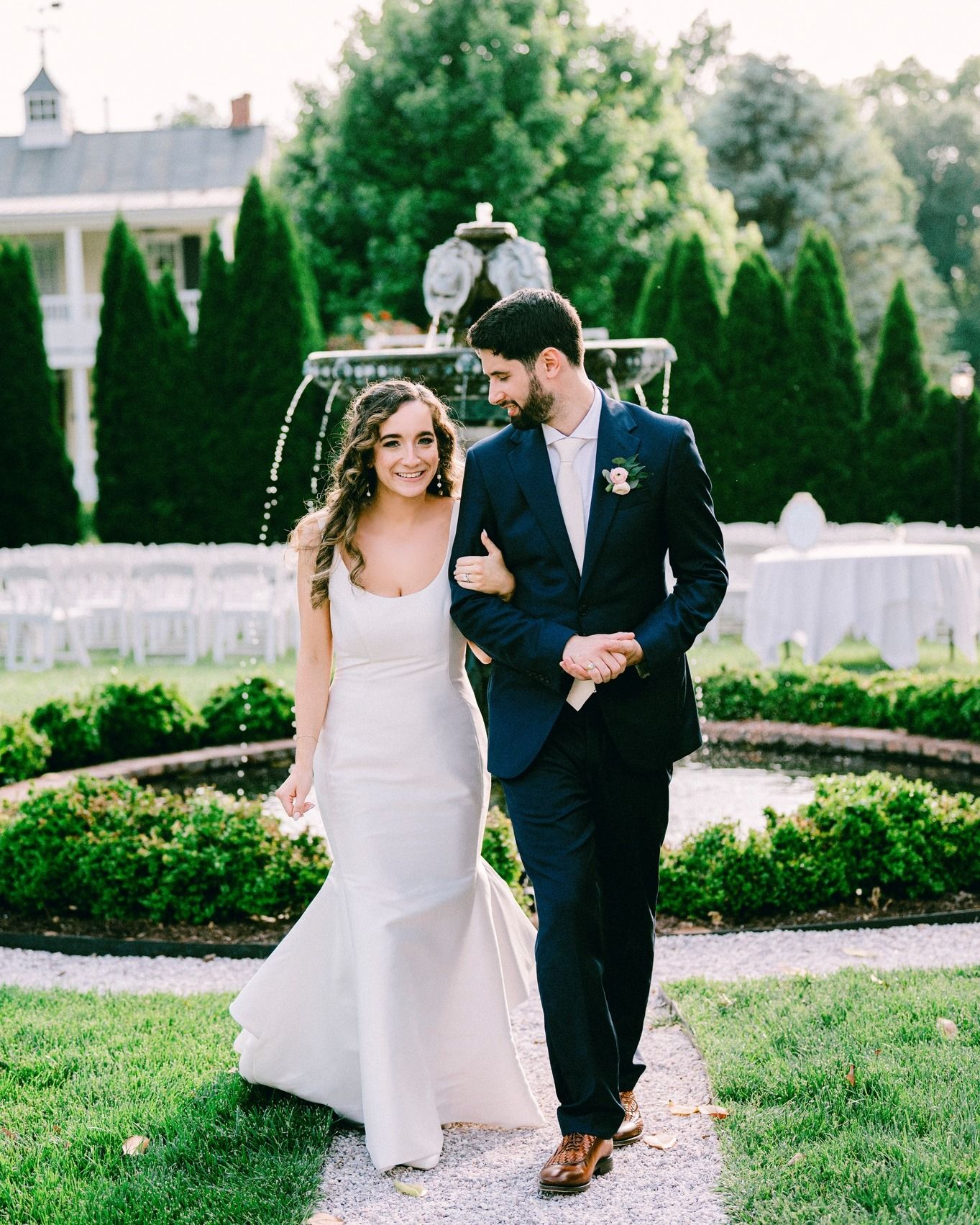 A bride and groom walk together through an elegant garden with manicured hedges and white flowers at Maryland wedding venue Antrim 1844.