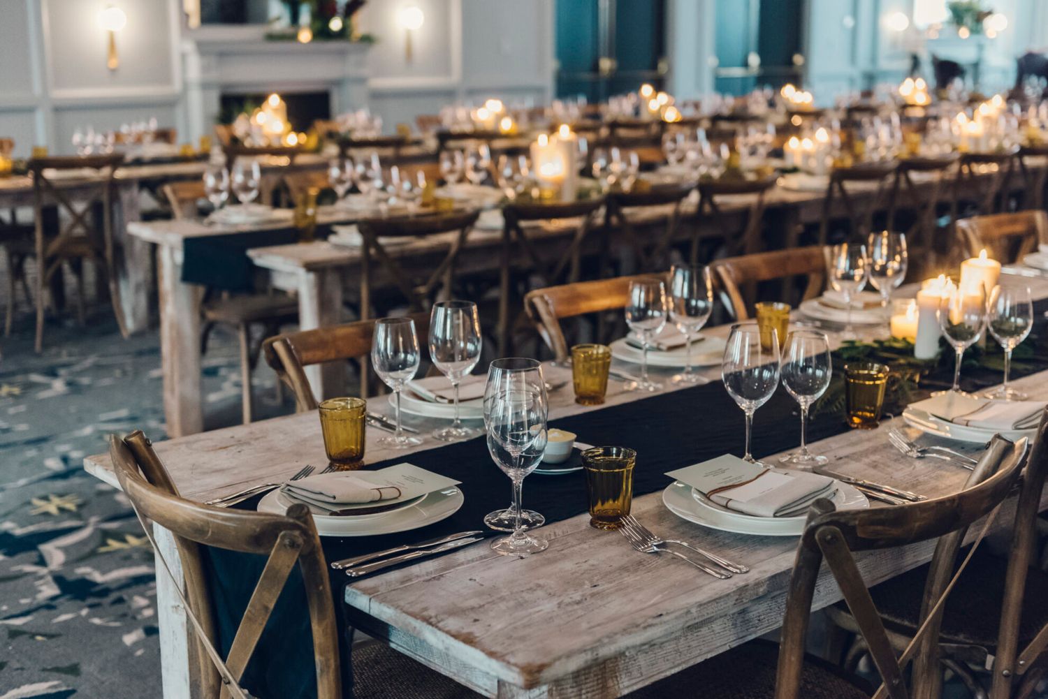 Elegant rustic reception tables set with wine glasses and place settings on wooden farmhouse tables in a teal themed room.