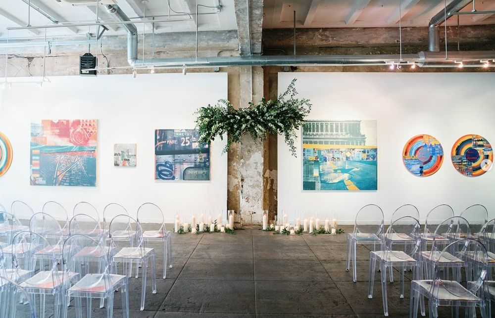 A panoramic view of an industrial office space with exposed ceiling, white walls, and hanging artwork displays.