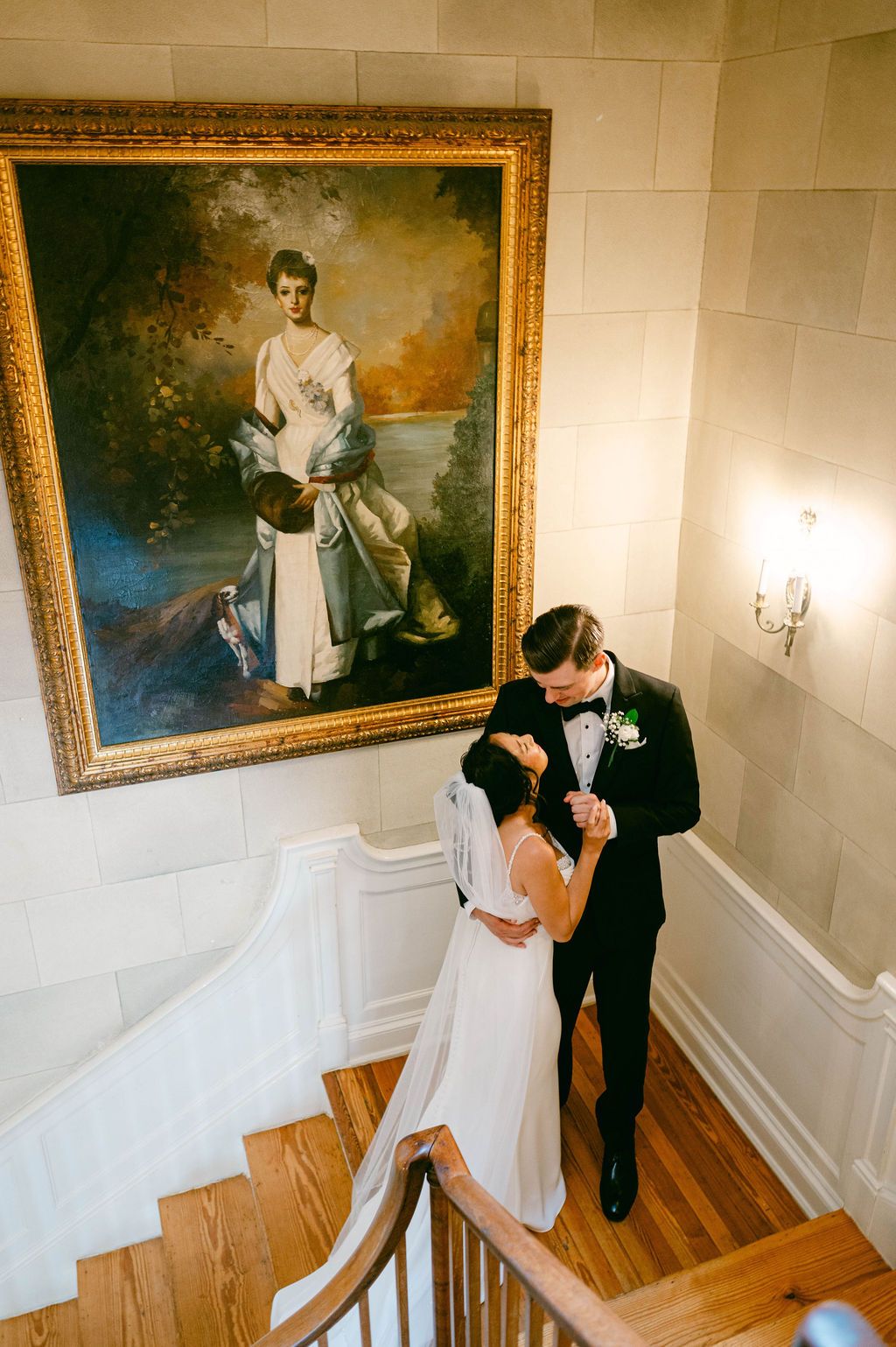 Wedding couple shares an intimate moment in an elegant room with ornate gold-framed artwork and hardwood floors at the Belmont Country Club.