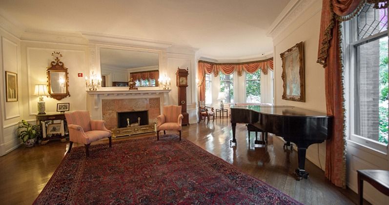 Elegant living room with grand piano, ornate fireplace, and large Persian rug in traditional decor.